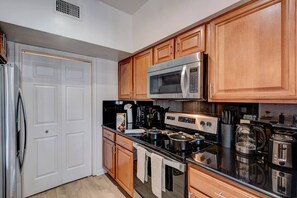 A modern kitchen with stainless steel appliances, wooden cabinets, and a black countertop. - 2BD Pumpkin King Retreat |NRG & TMC| Pool & Patio (Houston)