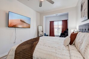 Habitación de hotel con una cama grande, televisor de pantalla plana en la pared, sillón de masaje y una ventana con cortinas.