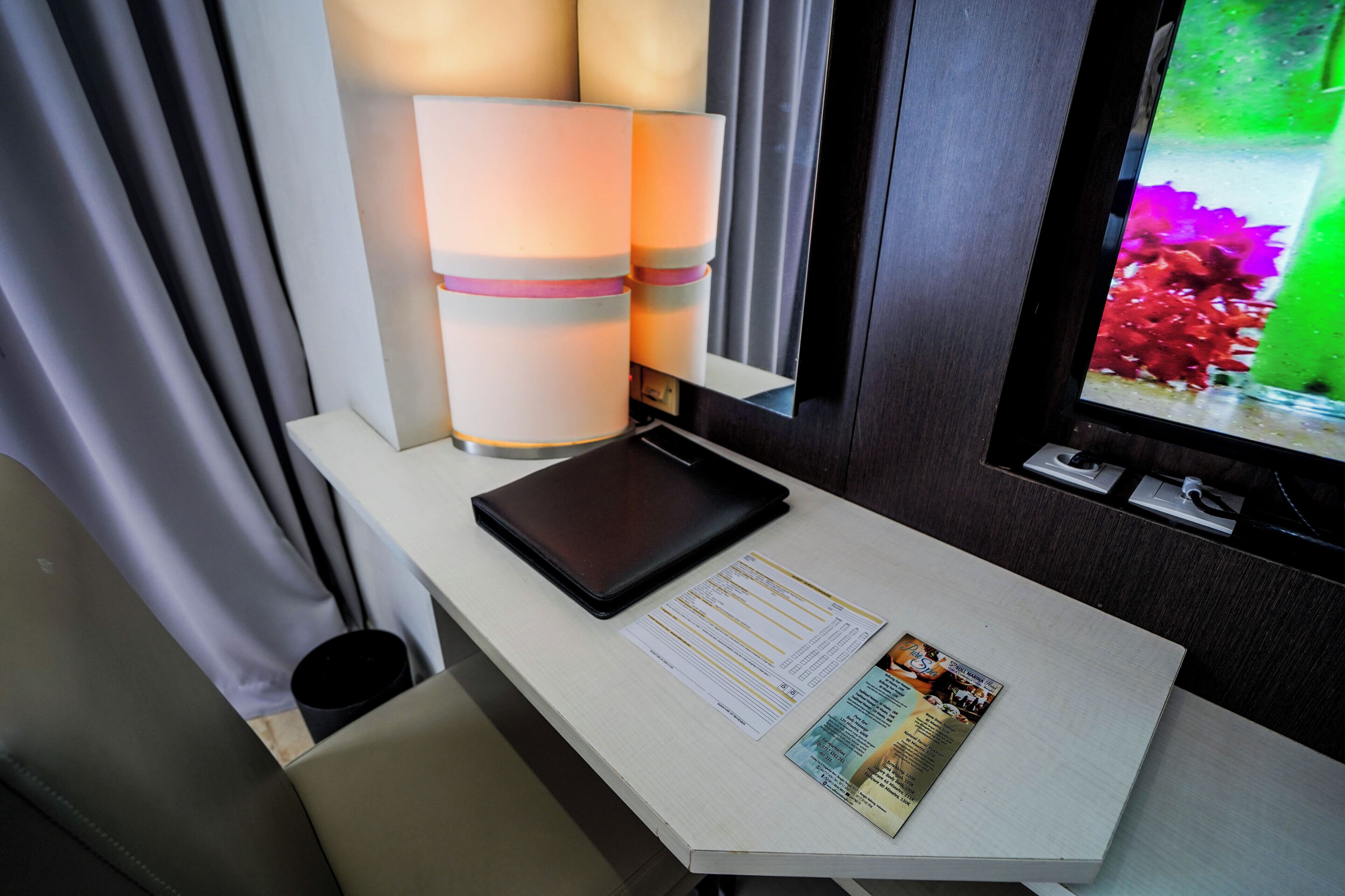 A hotel room with a desk, a tablet, a menu, and a window with a view of flowers.