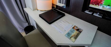 A hotel room with a desk, a tablet, a menu, and a window with a view of flowers.