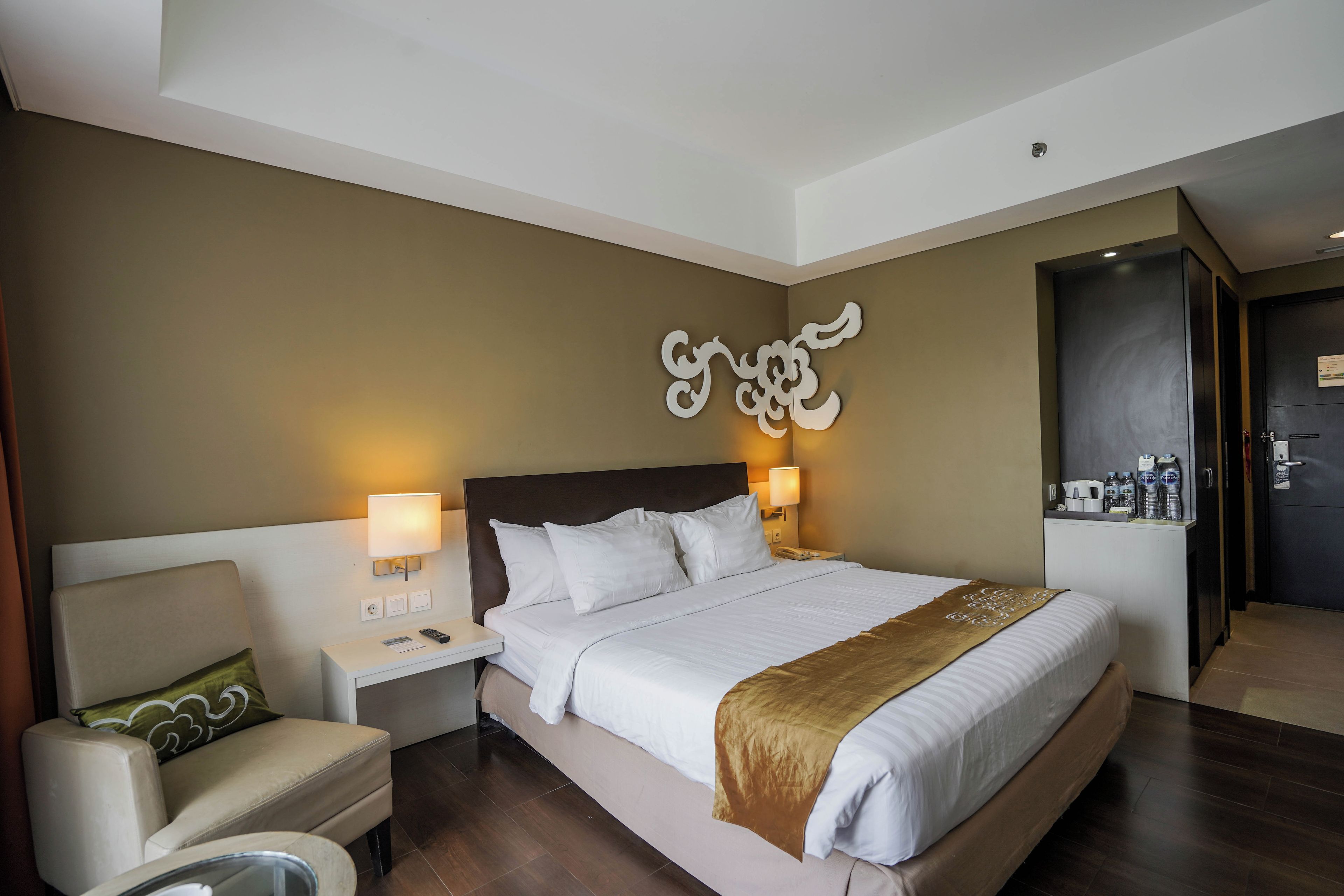 A hotel room with a large bed, two bedside lamps, a chair, a desk, and a wall-mounted decorative piece.