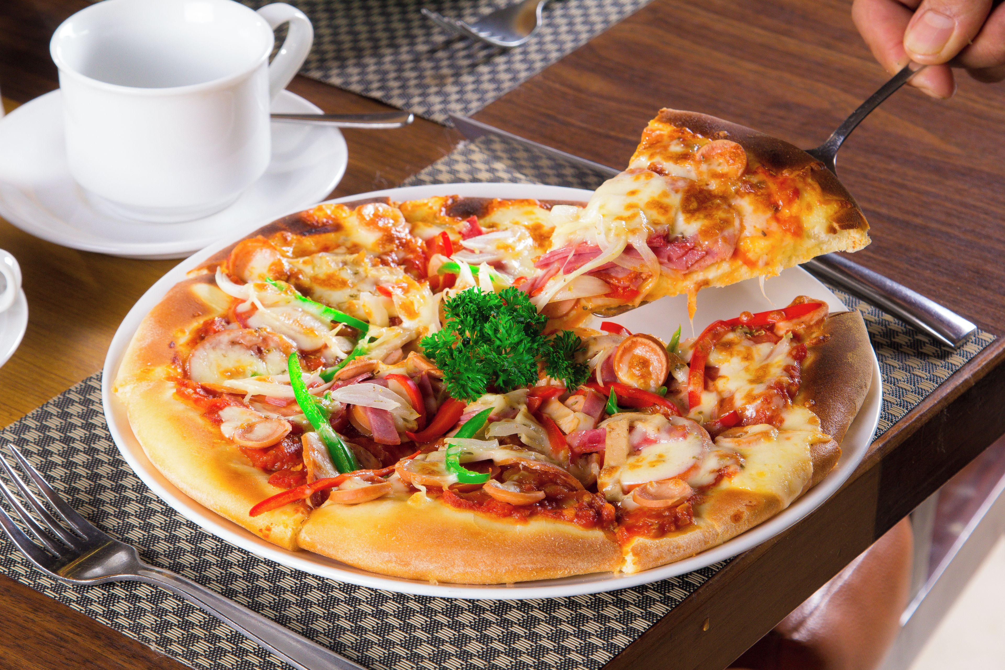 A pizza with various toppings on a white plate, accompanied by a cup and a fork on a table.