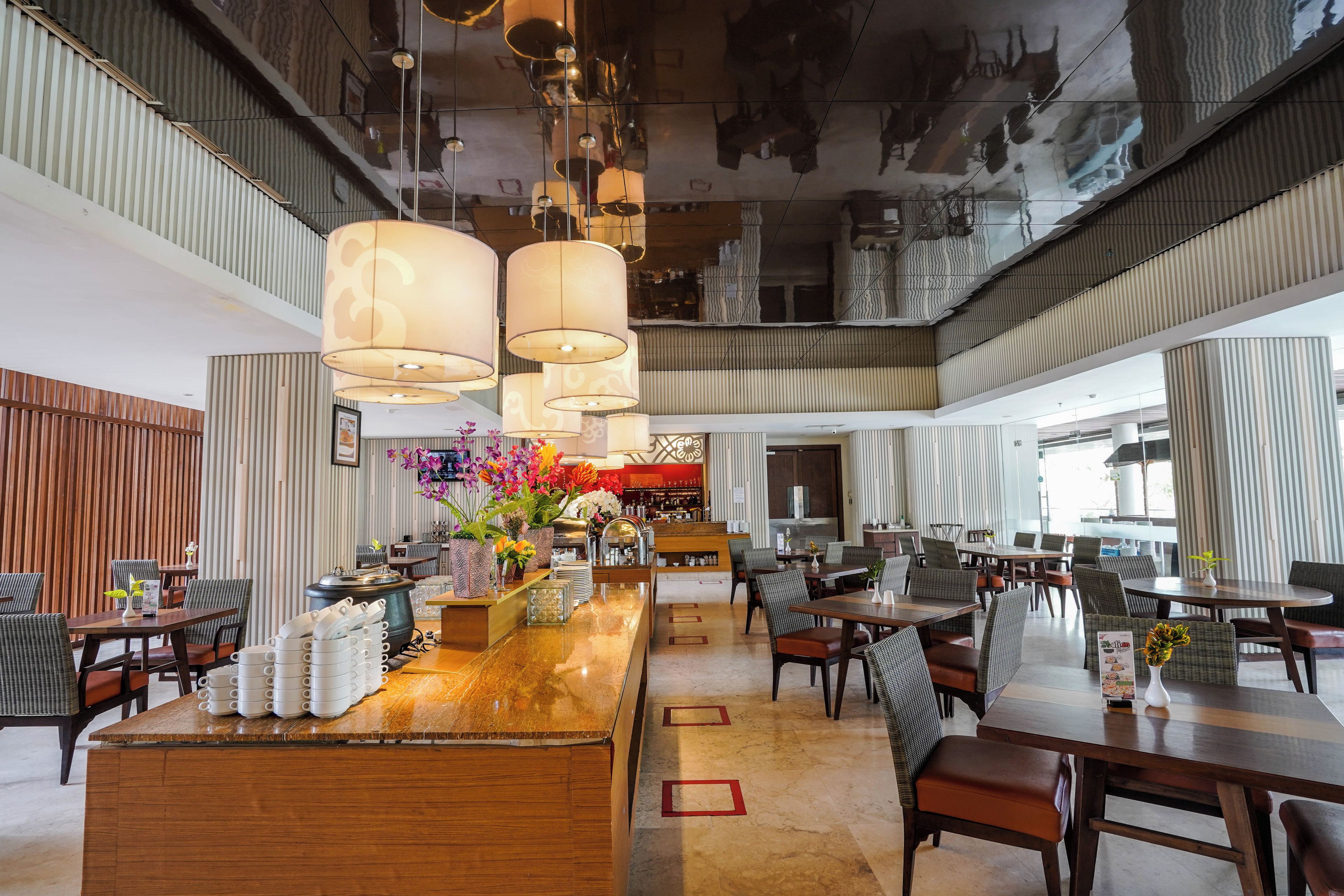 Un hall d’hôtel spacieux avec un bar central, des espaces aménagés pour s’asseoir et un design moderne au niveau du plafond.