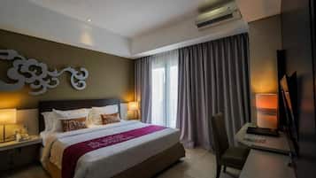 Quarto de hotel com cama, abajures, escrivaninha com cadeira, televisão de tela plana e uma grande janela com cortinas.