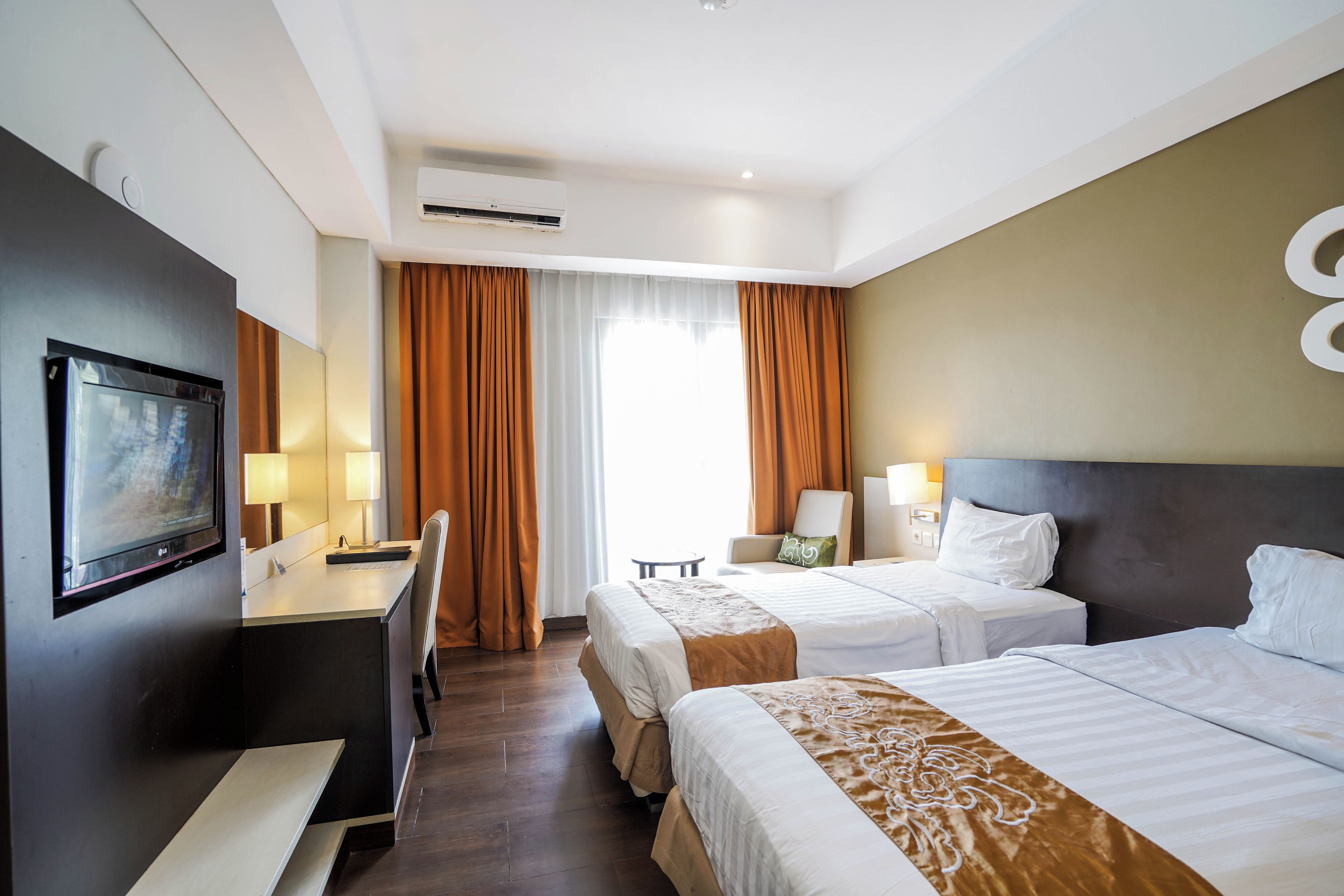 A hotel room with a bed, bedside table, lamp, desk with chair, and a television.