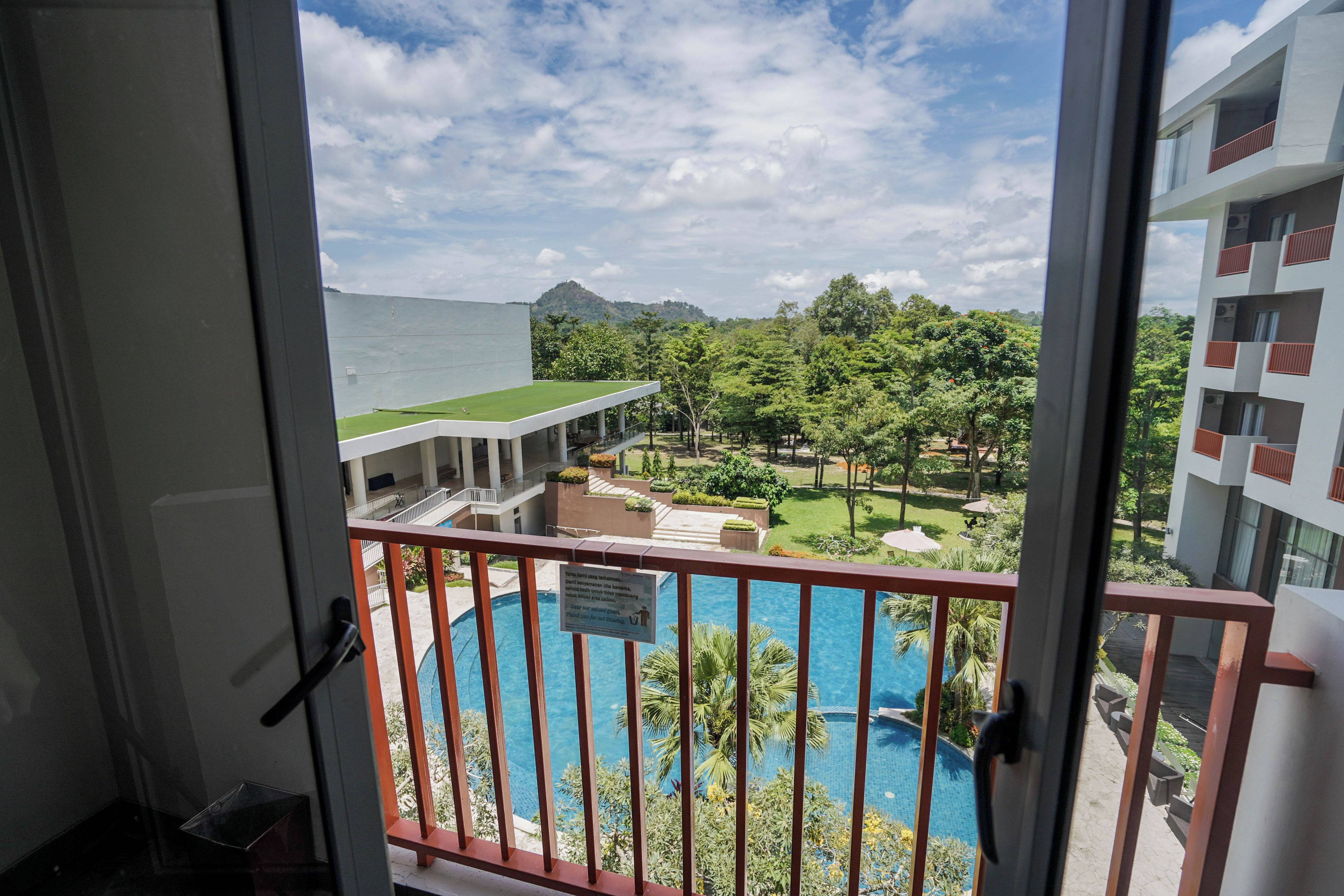 Un balcón con vista a una piscina, un edificio con techo plano y un paisaje montañoso al fondo.