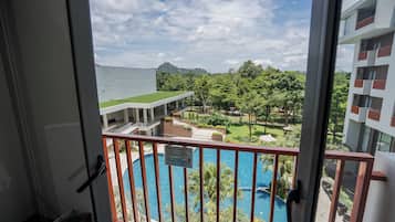 Un balcón con vista a una piscina, un edificio con techo plano y un paisaje montañoso al fondo.