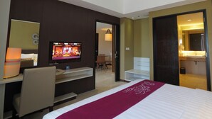 Habitación de hotel con cama, televisor, escritorio y baño visible a través de una puerta abierta.
