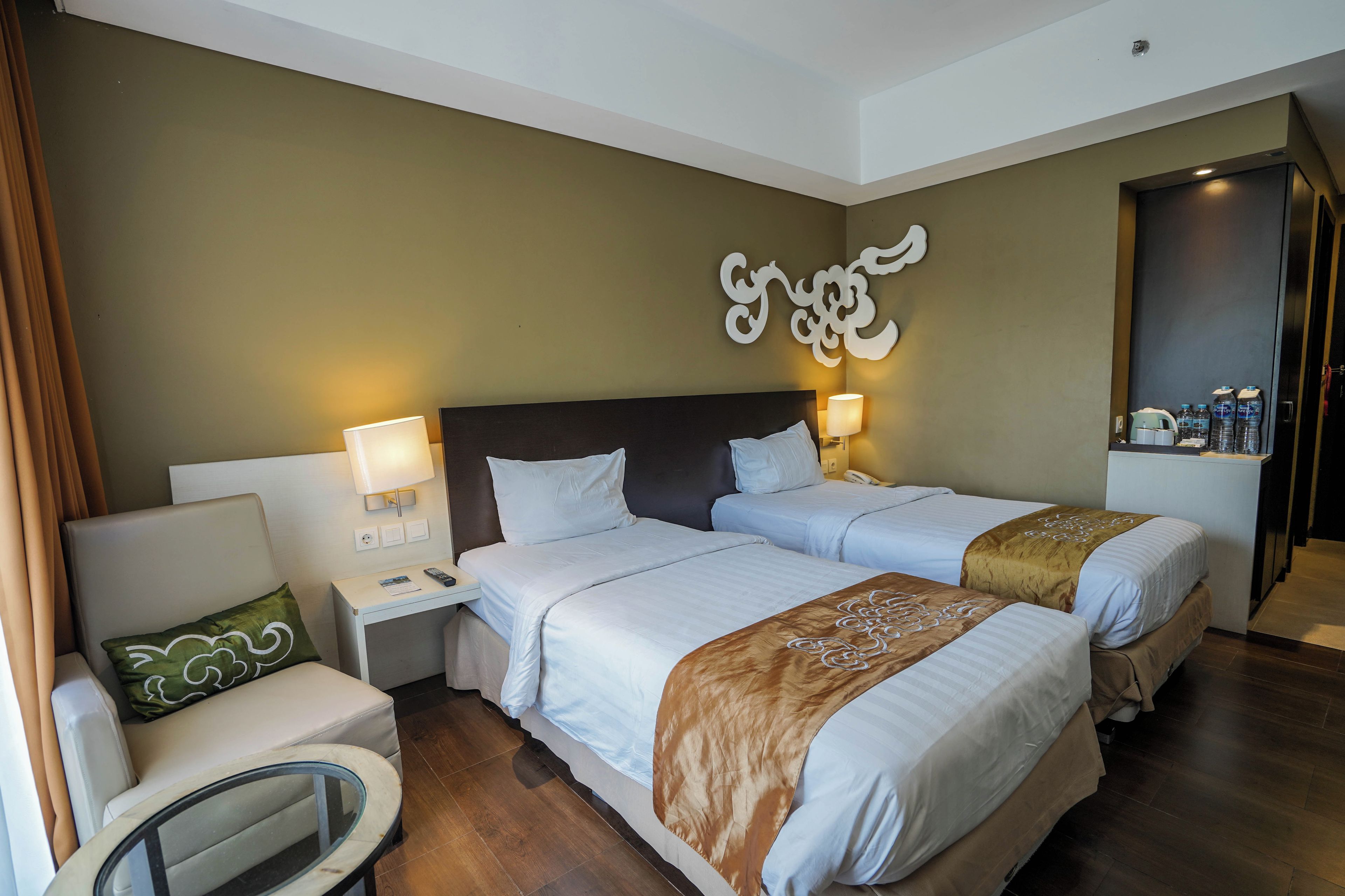 Une chambre d’hôtel avec deux lits, une table de chevet, une chaise et un élément décoratif fixé au mur.