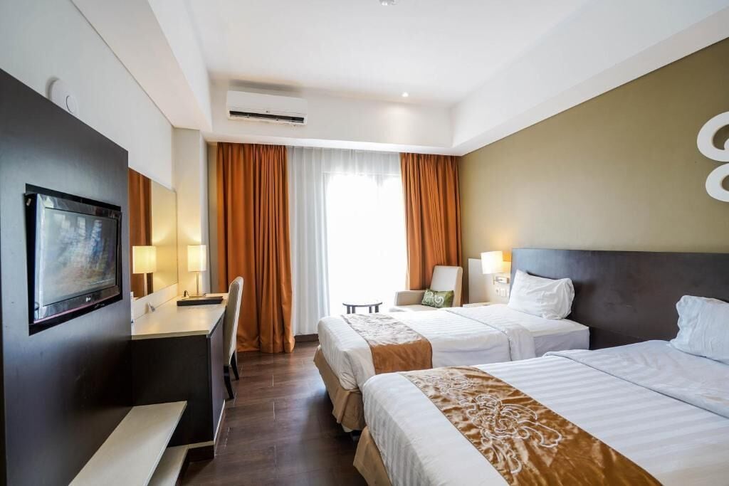 A hotel room with two beds, a desk, a chair, a television, and a window with curtains.
