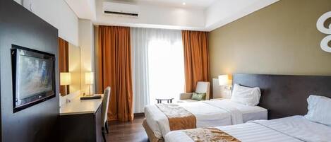 A hotel room with two beds, a desk, a chair, a television, and a window with curtains.