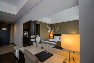 Una habitación de hotel con cama, mesita de noche, lámpara y televisor.
