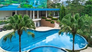Área de piscina com duas piscinas circulares, palmeiras e um edifício com um mural.