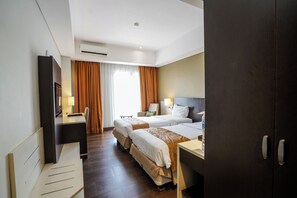 A hotel room with two beds, a desk, a chair, a TV, and an air conditioning unit.