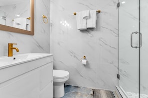 Ein modernes Badezimmer mit einem weißen Marmorwaschtisch, goldenen Armaturen, einer Toilette und einer Duschkabine aus Glas.