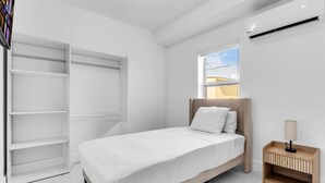 A bedroom with a bed, a wooden nightstand, a white wardrobe, and a window with a view. - Cozy 2-bedroom apartment with AC and kitchen, Tavernier (Tavernier)