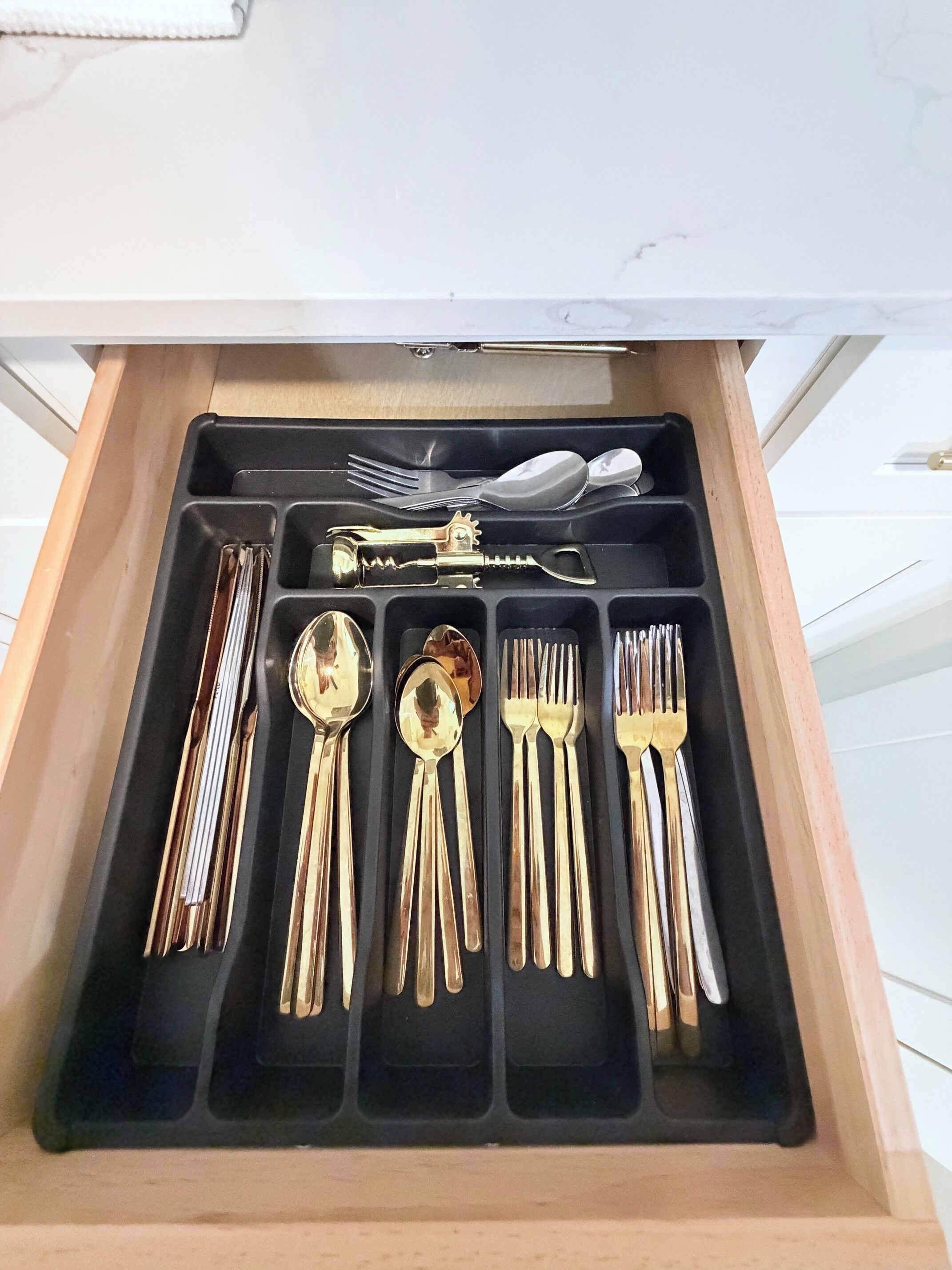 A drawer with compartments containing various utensils including forks, spoons, and a bottle opener.