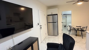 A modern living room with a flat-screen TV, black sofa, and a dining area with a table and chairs. - Cozy 2-bedroom apartment with AC and kitchen, Tavernier (Tavernier)