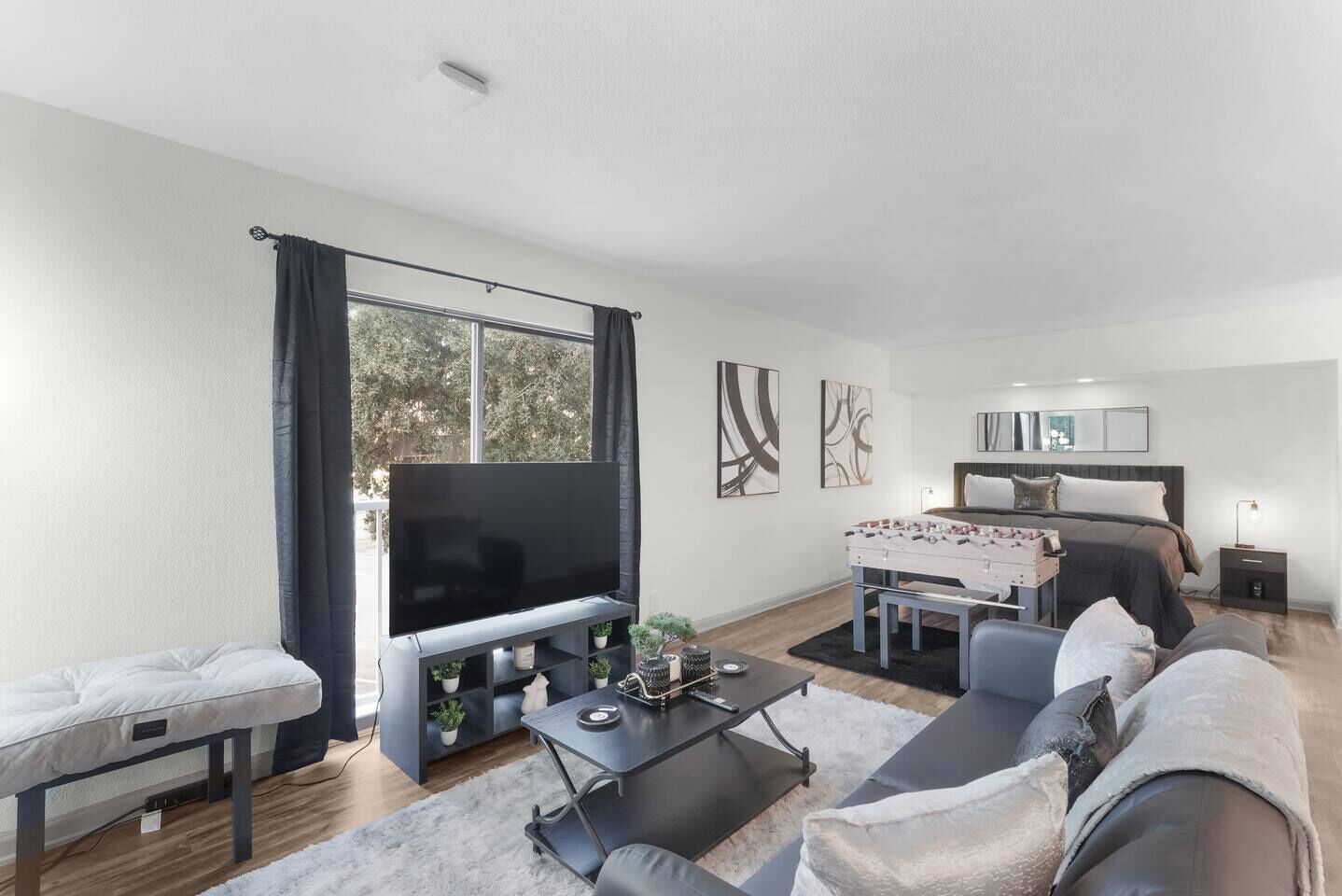 A modern living room with a flat-screen TV, sofa, coffee table, and a dining area with a table and chairs.