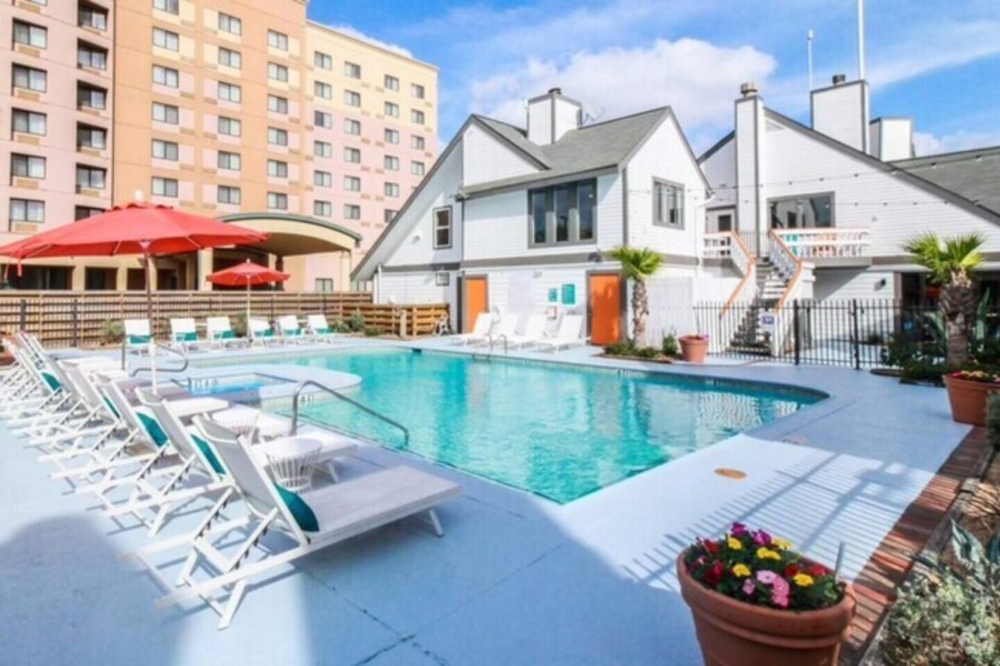 A swimming pool with lounge chairs and umbrellas, surrounded by buildings.