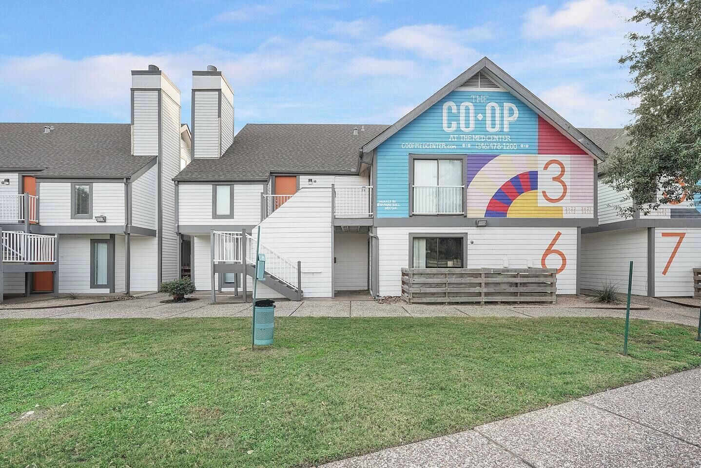 A residential building with a colorful mural on the side, a visible number '3' on the facade, and a small outdoor seating area.