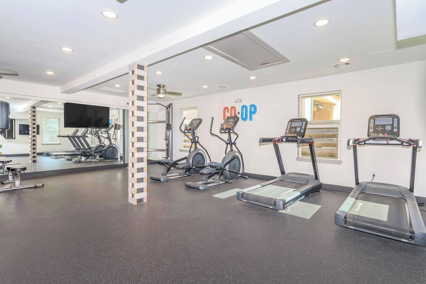 Ein Fitnessraum mit Laufbändern, Crosstrainern und einer Spiegelwand.
