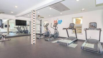 Ein Fitnessraum mit Laufbändern, Crosstrainern und einer Spiegelwand.
