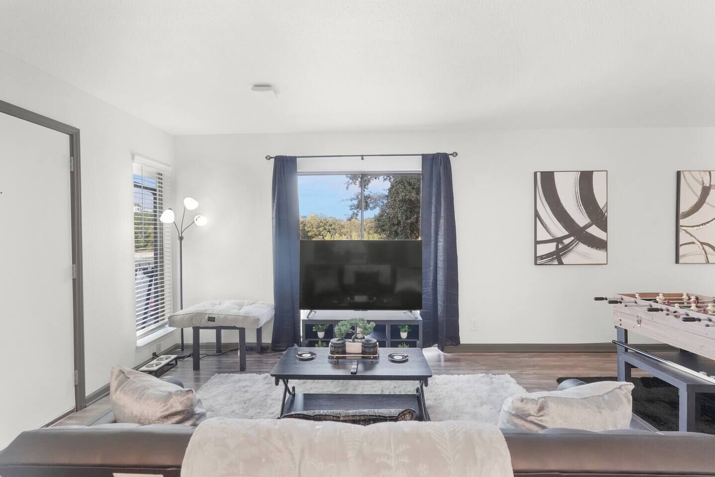Ein Zimmer mit einer Couch, einem Tisch mit einem Flachbildfernseher, einem Kicker und Bildern an der Wand.