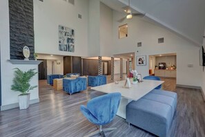 A spacious living area with a high ceiling, a dining table with blue chairs, and a kitchen in the background. - Luxe 1BR Retreat |Pool & Hot Tub| TMC & NRG| Rodeo (Houston)