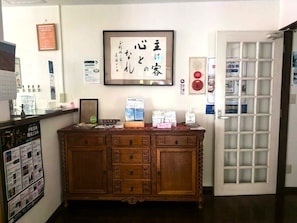 A reception area with a wooden cabinet, framed calligraphy, and various informational posters. - Vrbo Property (伊東市)