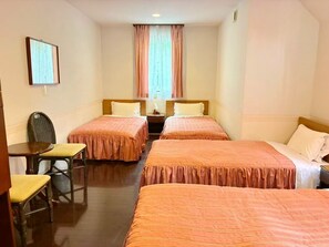 A hotel room with two single beds, a small table with a chair, a nightstand, and a window with curtains. - Vrbo Property (伊東市)