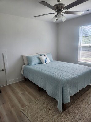 Ein Schlafzimmer mit einem Bett, einem Deckenventilator, einem Fenster mit Jalousien und einer Tür.