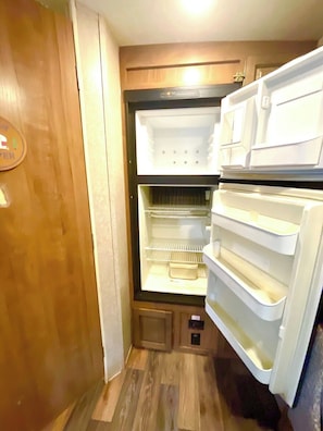 A compact refrigerator with multiple shelves and a freezer compartment, located in a small kitchen area with wooden flooring and cabinetry. - Surprisingly Comfy RV with Everything You Need (Jacksonville)
