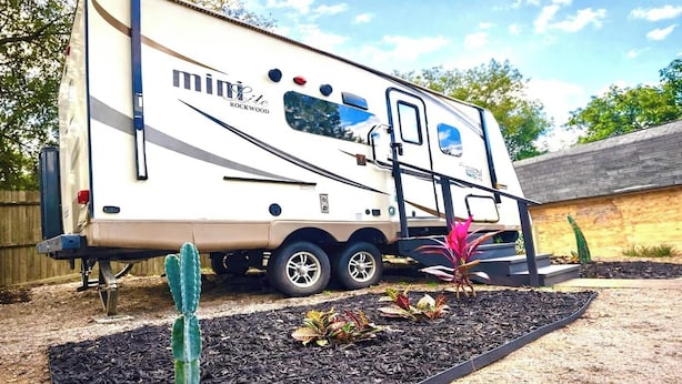 A recreational vehicle with a 'minibeast rockwood' logo, a ladder, and a small garden area with plants and mulch. - Surprisingly Comfy RV with Everything You Need (Jacksonville)