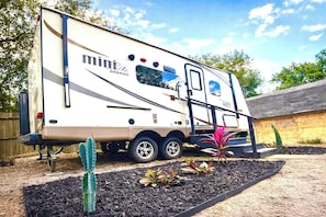 A recreational vehicle with a 'minibeast rockwood' logo, a ladder, and a small garden area with plants and mulch. - Surprisingly Comfy RV with Everything You Need (Jacksonville)