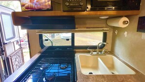 A compact kitchenette with a stove, sink, and a TV mounted above the stove. - Surprisingly Comfy RV with Everything You Need (Jacksonville)