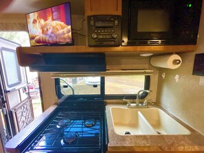 Cozinha compacta com fogão, pia e televisão instalada acima do fogão.