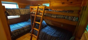 A bunk bed room with a wooden ladder, two beds with striped bedding, and a window.