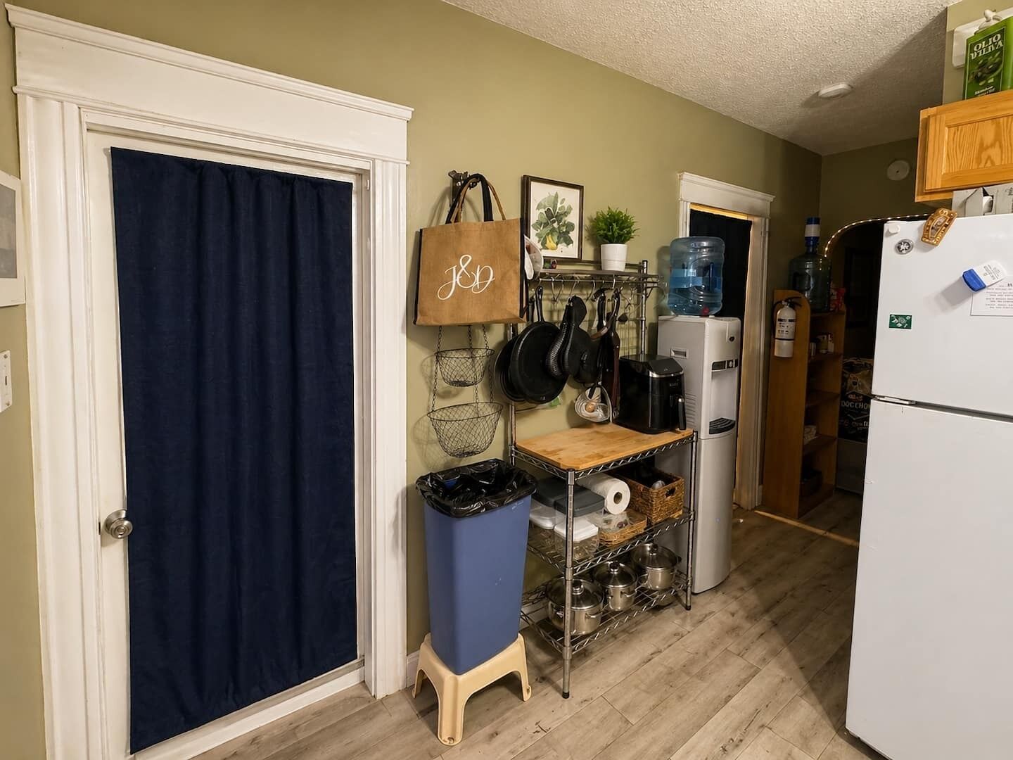 Una cocina con refrigerador, dispensador de agua, cafetera y estante con ollas y sartenes.