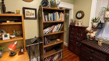 Quarto com estante de madeira repleta de livros, escrivaninha com luminária, globo terrestre e relógio na parede.