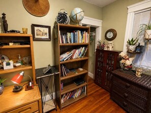 Quarto com estante de madeira repleta de livros, escrivaninha com luminária, globo terrestre e relógio na parede.