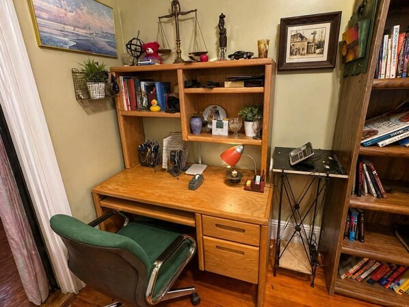 Uma mesa de madeira com uma cadeira verde, uma lâmpada e diversos objetos, incluindo livros, uma balança e um urso de pelúcia.