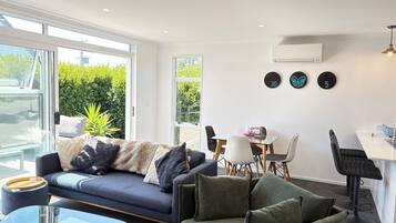 A modern living room with a sofa, a glass coffee table, and a dining area with chairs and a table.