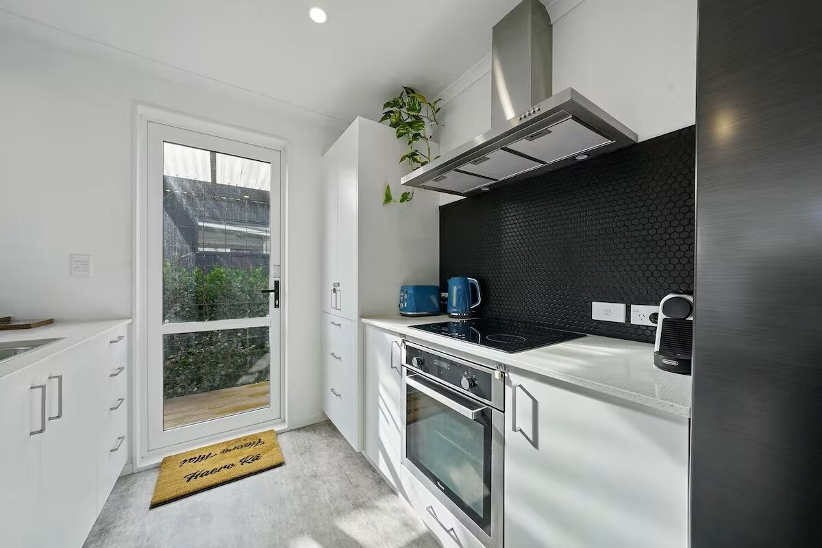 Cozinha moderna com painel de fundo preto, eletrodomésticos de aço inoxidável e porta de vidro deslizante que dá para uma varanda.