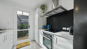 Cozinha moderna com painel de fundo preto, eletrodomésticos de aço inoxidável e porta de vidro deslizante que dá para uma varanda.