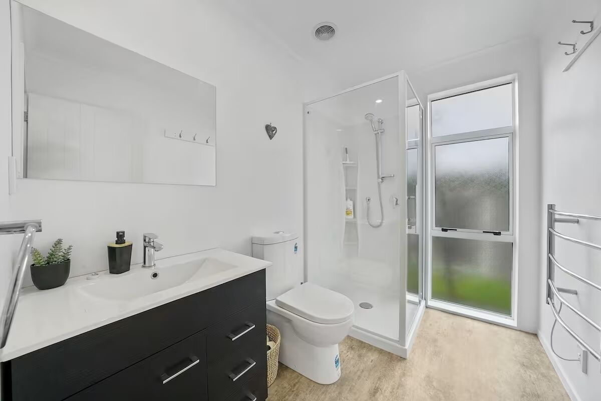 A modern bathroom with a white sink, black vanity, a toilet, and a glass-enclosed shower area.