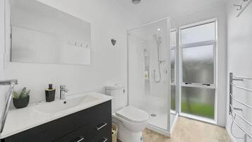 A modern bathroom with a white sink, black vanity, a toilet, and a glass-enclosed shower area.