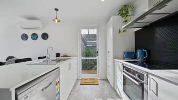 A modern kitchen with white cabinetry, a stainless steel range hood, and a black backsplash.