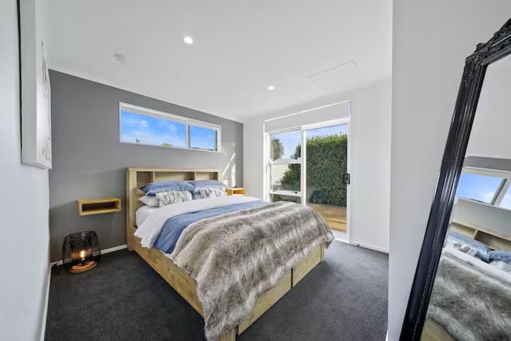 Quarto com uma cama grande, mesa de cabeceira, espelho e vista para o exterior.