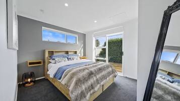 Quarto com uma cama grande, mesa de cabeceira, espelho e vista para o exterior.